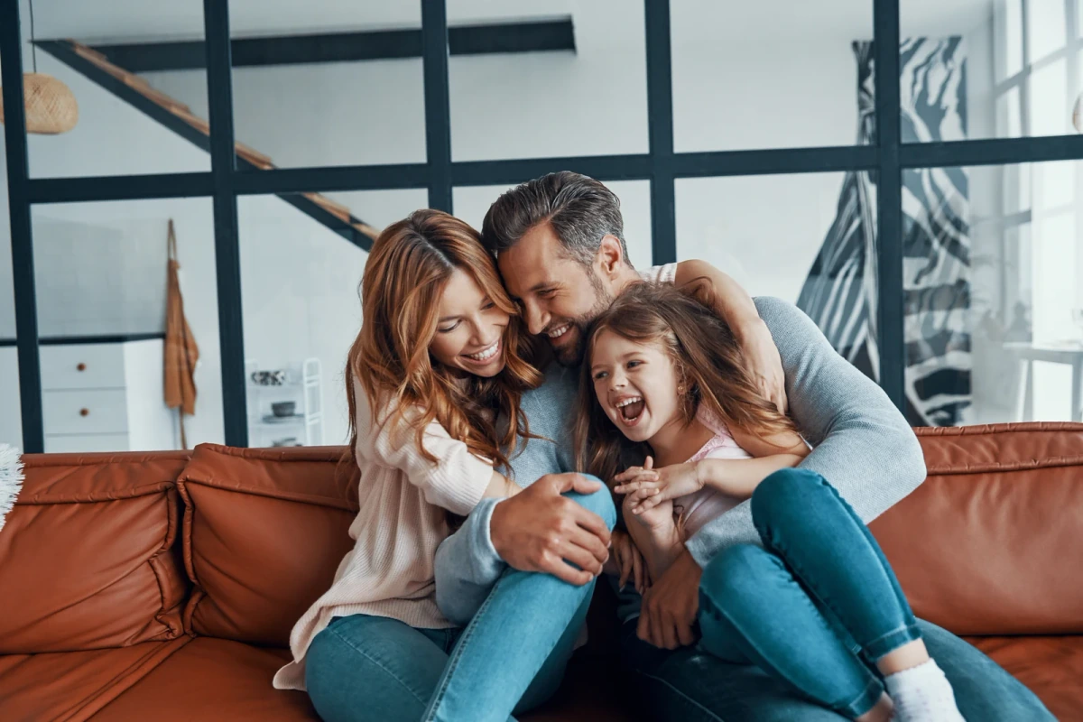 Two parents laughing with their daughter on a sofa