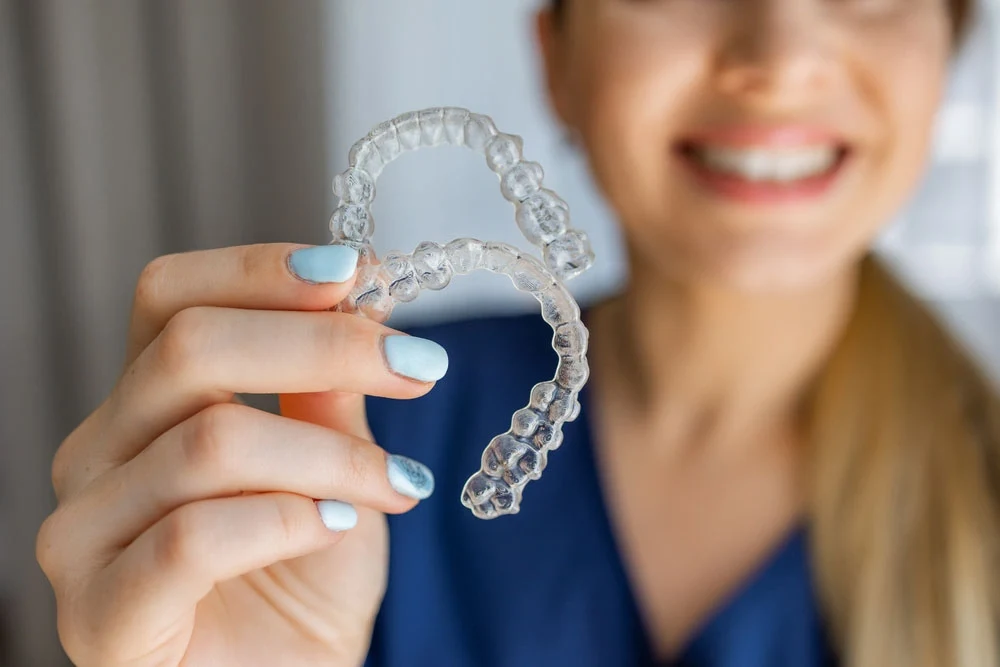 A smiling woman holding clear dental aligners