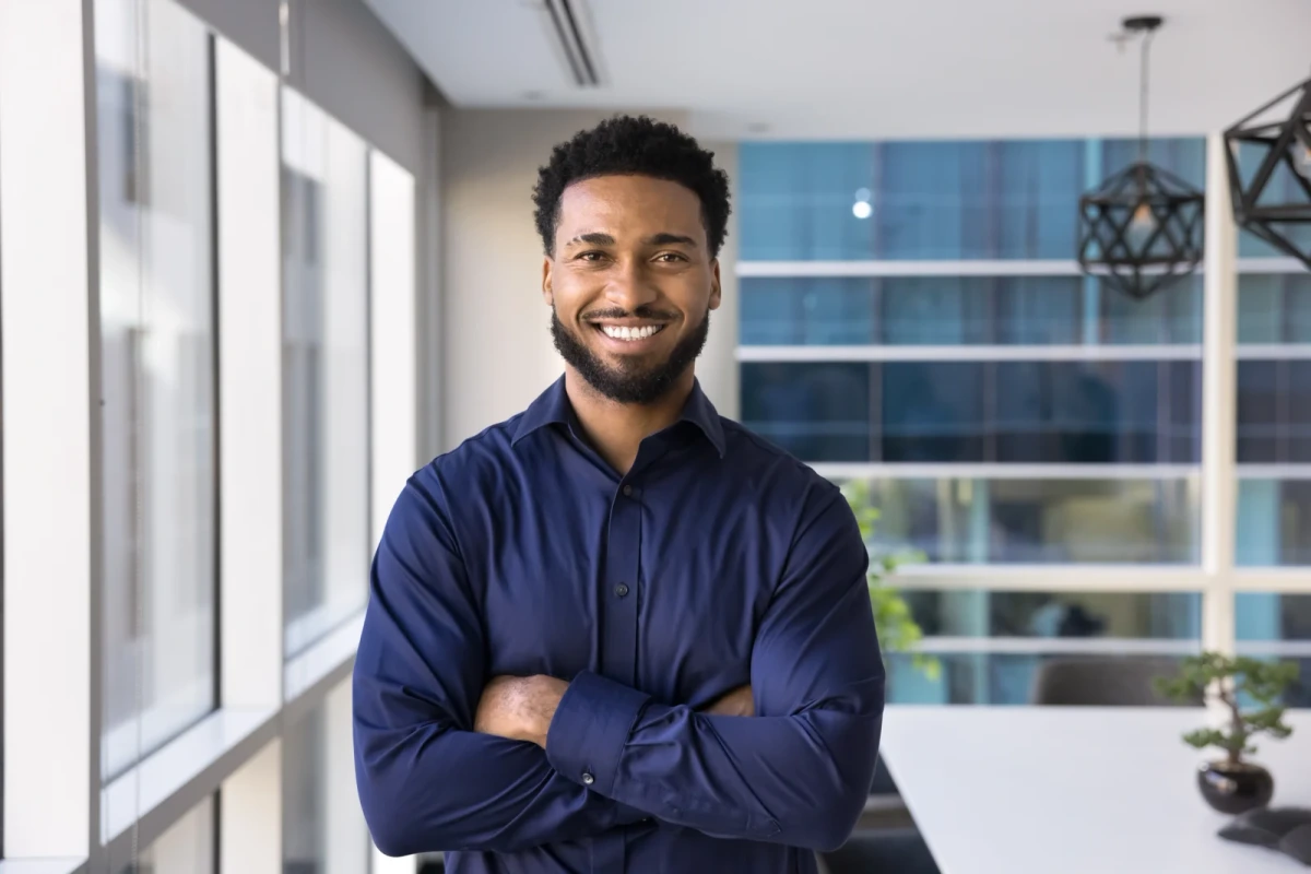 A smiling man wearing a navy shirt beside a window