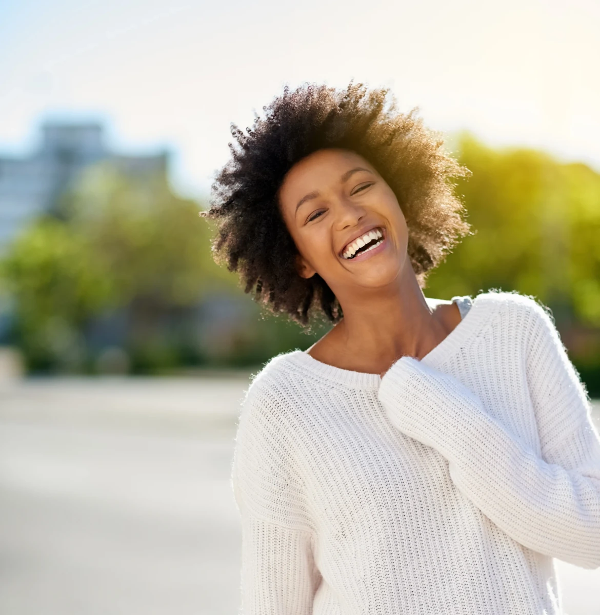 A smiling woman with curly hair wearing a white sweater outdoors