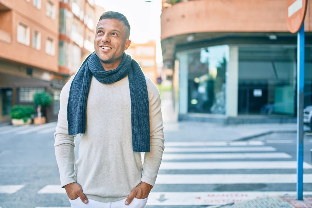 A smiling man in a cream sweater and blue scarf outdoors