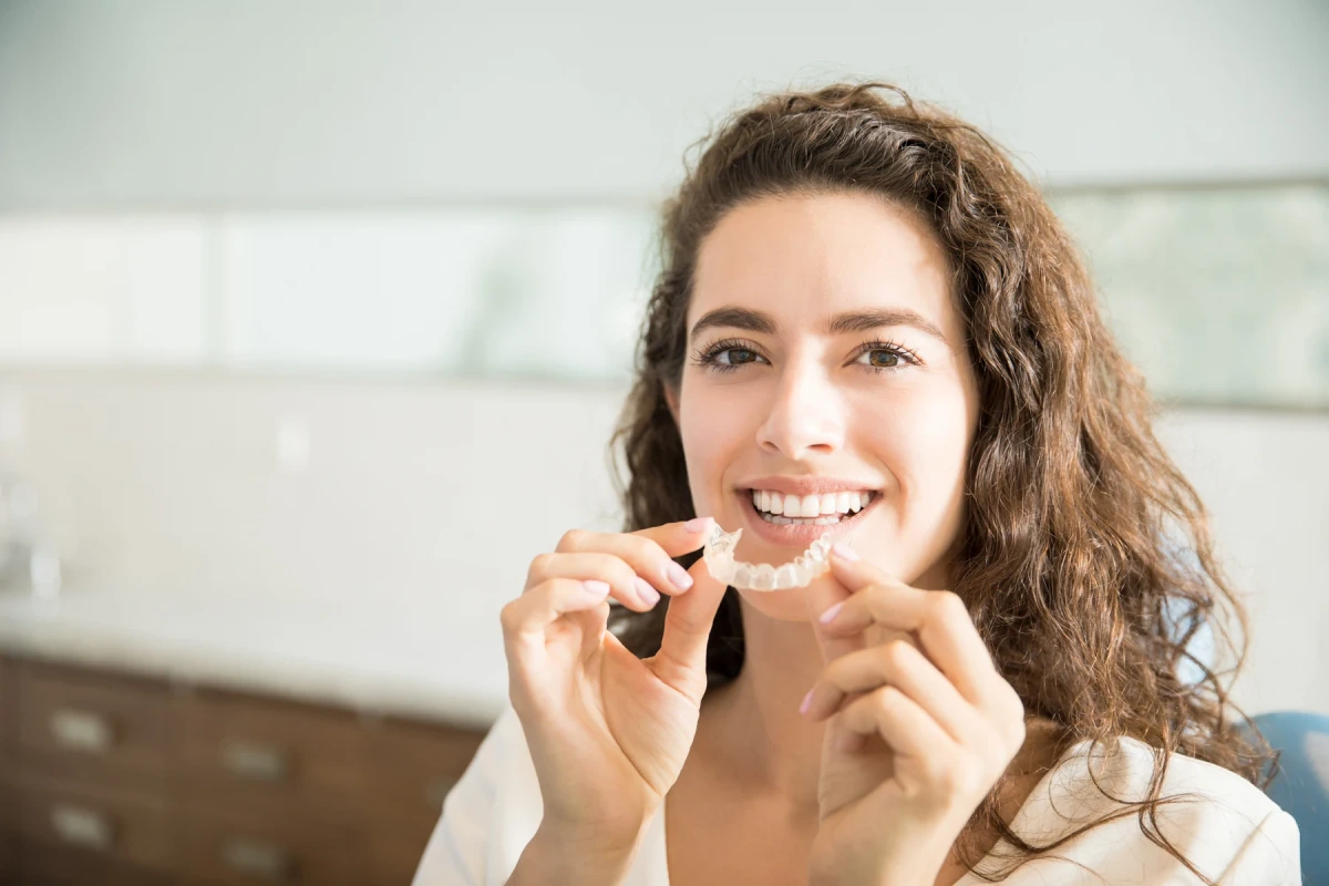 A smiling woman holding a clear dental aligner