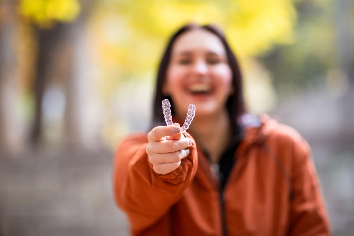 A smiling woman holding a clear dental aligner